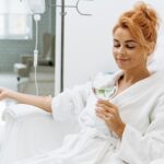 Side view portrait of charming woman in white bathrobe sitting in armchair and holding glass of lemon water. | Estevez Aesthetics in Las Vegas, NV